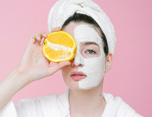 A woman wearing a face mask holds an orange, symbolizing the importance of vitamin C in skincare routines.