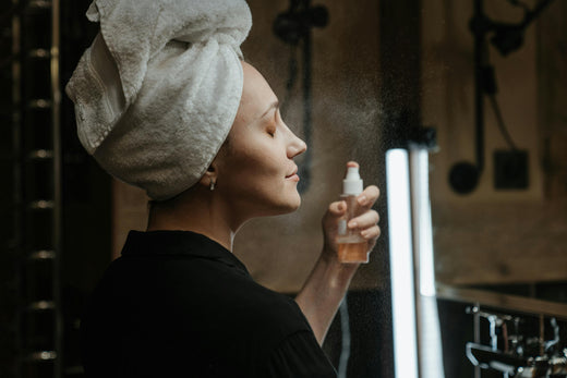 A woman with a towel on her head holds a spray bottle, emphasizing the significance of toner in skincare routines.